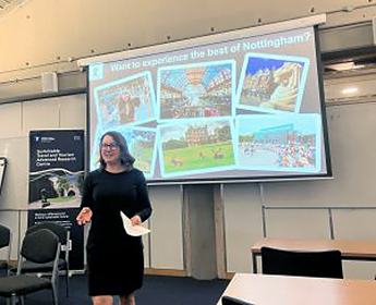 Jillian Rickly presenting at the STTAR Centre World Tourism Day 2025. Jillian is stood in front of a projector screen in a seminar room. The screen is showing various images depicting tourism.