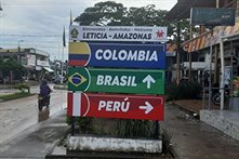 Street sign indicating the boarder of Leticia, Colombia and Tabatinga and Brazil. The top is black letters on a white board saying 'Leticia - Amazonas. Underneath that is a blue board with white letters saying 'Colombia' and the flag colours to the left o