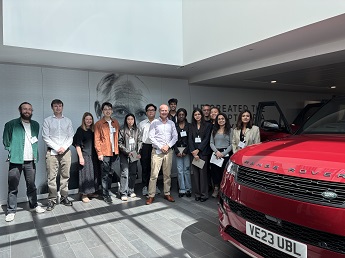 Photo of the participants of the MSc Consultancy Competition - 2025, visiting Jaguar Land Rover. There is the bonnet of a red Range Rover in the foreground of the photo to the right, with the participants stood in the background.
