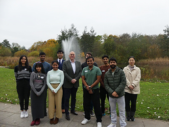 Photo of the Sustainability and Societal Impact Fellows stood with David Park in front of a fountain on Jubilee Campus.
