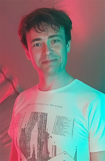 An informal head and shoulders photo of Brendan Canavan. Brendan is in a white t-shirt with a graphic printed on the front. He is looking at the camera and smiling.