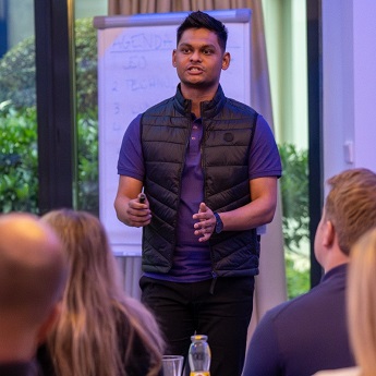 Kaustubh Nande wearing a black gilet, standing in front of a large pad on a stand, presenting to people sitting down facing him