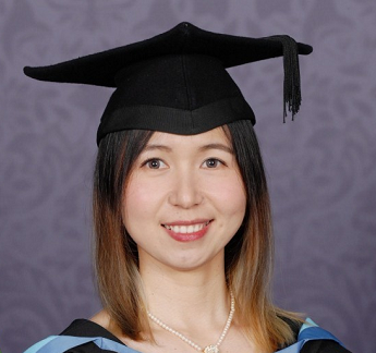 Xiaoli Fu (Sherry) smiling, short brown highlighted hair, wearing a black graduation hat and gown with blue trim in front of a dark swirly grey background.