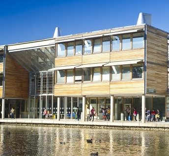 Wooden and glass buildings on Jubilee Campus behind the lake, blue skies