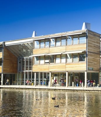 Wooden and glass buildings on Jubilee Campus behind the lake, blue skies