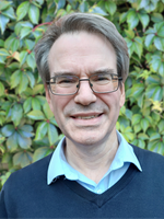 Head and shoulders photo of Stephen Timmons. Stephen is wearing glasses, a navy jumper and a light blue shirt.