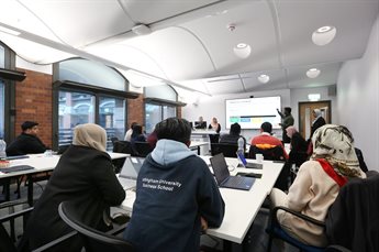 Members of the Digital Leadership and Innovation for Public Sector Transformation programme sit around tables listening to a group presentation.