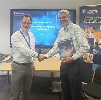 Keithith Burgess shakes hands with a Uniper programme participant. They both smile at the camera and the participant holds his participation certificate.