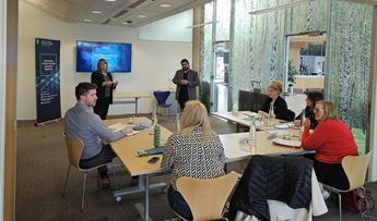 Programme participants from Midlands Engine sit around tables during a workshop. Aditya Jain and Julie Blant stand at the front of the room listening while the participants discuss ideas.