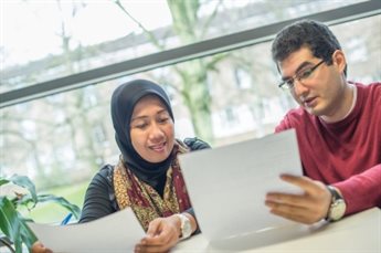 A man and a woman look at documents in a bright room.
