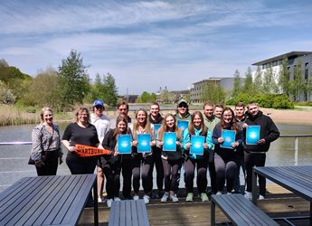 Group photo of Wartburg college students and staff holding participation certificates in front of Jubilee lake.