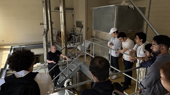 students at Castle Rock Brewery standing on balcony with metal pipes adn machinery in the background