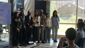 MSc Company Consultancy Competition presentation. Team for Radiant Cleaners, winners standing in front of a large banner holding a silver trophy: Mentor Professor Andrew Bacon, Business partner Adam Kirkup, students Cui Wanhe, Dominic Paul, Fiza Iqbal, Ni