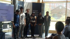 MSc Company Consultancy Competition presentation. Team for Radiant Cleaners, runners up standing in front of a large banner: Mentor Professor Andrew Bacon, Business partner Adam Kirkup, Debadrita Roy, Monish Mokka, Omer Bicimveren, Shubham Vijay Thakkar, 