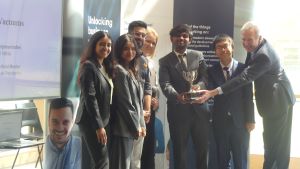 MSc Company Consultancy Competition presentation. Team for Busch Vacuums, runners up standing in front of a large banner holding a silver trophy: Mentor David Pemberton, Business partner Garvit Mehta, students Anthony-Earl Diallo, Bhumika Mina, Jin Li, Kr