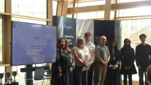 MSc Company Consultancy Competition presentation. Team for Jaguar Land Rover, runners up standing in front of a large banner: mentor Professor Andrew Callaghan from Business School, Business partner Lee Cooper-Blair, students Haya Jafri, Imamura Yuma, Li 
