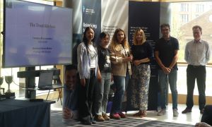MSc Company Consultancy Competition presentation. Team for The Treat Kitchen, runners up standing in front of a large banner: mentor Professor Professor Keith Burgess from Business School, Business partners Jess Barnett and Lydia McDonald, students Jiawen