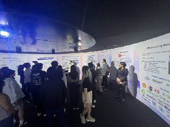 MSc Digital Marketing students standing in a group in a dark room in front of white display boards on a visit to IBM Client Innovation Centre