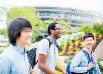 A group of male students smiling and walking past the Ingenuity Centre building