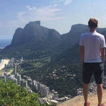 A man stands in shorts looking down at Rio Janerio and across at the famous mountainous landscape