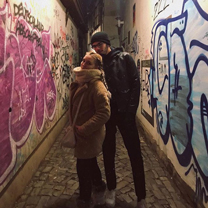 Two people stand wrapped against the cold in a narrow, graffitied alleyway