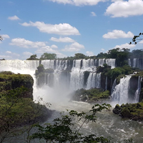 A massive waterfall in a tropical location under a blue sky with white fluffy clouds