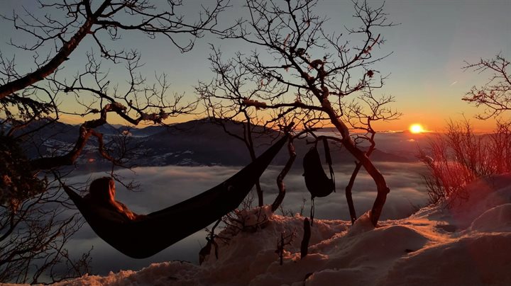 A photo of a person with long hair lying on a hammock on top of a snowy mountain.