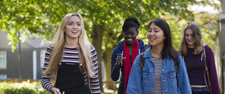 A group of four postgraduate students walk through the campus on a beautiful autumnal day