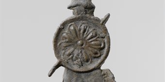 Side view of metal statue of a warrior bearing a round shield and spear and wearing a helmet