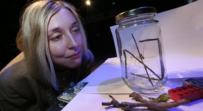Photo of Ellie Clifton looking at a  closed jar. In the jar is a spider