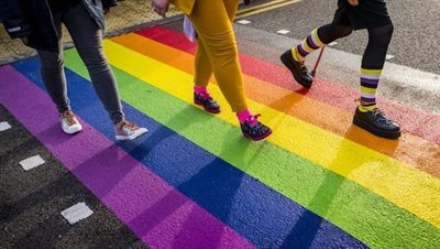 Photo of walking shot of three people walking over the rainbow zebra crossing