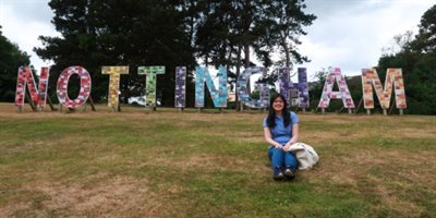 Photo of Vivien Lim sat on grass in front of Nottingham sign