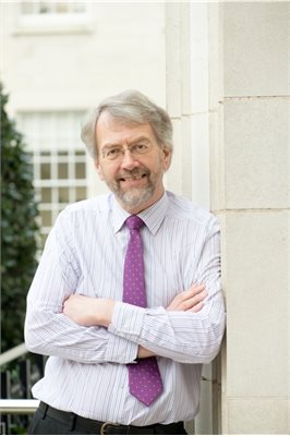 Professor John Beckett stands with his arms crossed outside a white building.