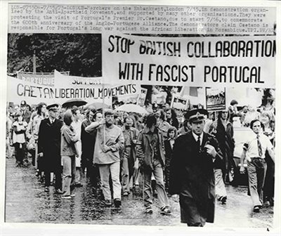 Black and white photo of people marching with banners in an anti-colonial demonstration in London.