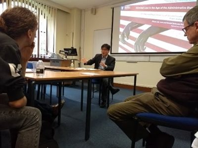 A presentation is delivered on a screen, in the seminar room the audience sit around tables.