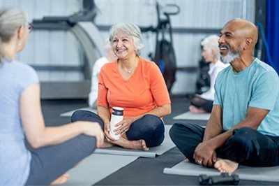Three older people with grey hair sat chatton yoga mats