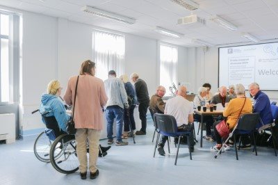 Room full of people talking and listening to each other with a presnetation in the background.