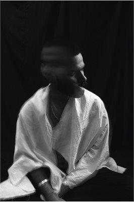 A black and white image of a seated man shaking his head and wearing a white shirt