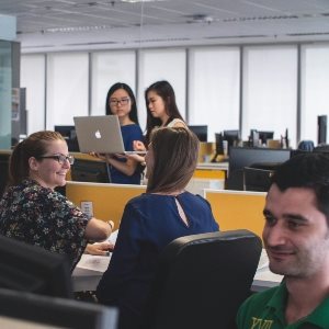 Two colleagues talking in an office with others in the foreground and background