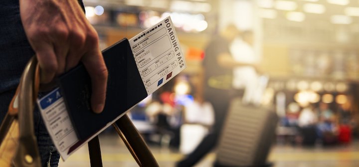 Close up image of a man holding a passport and a boarding pass in an airport