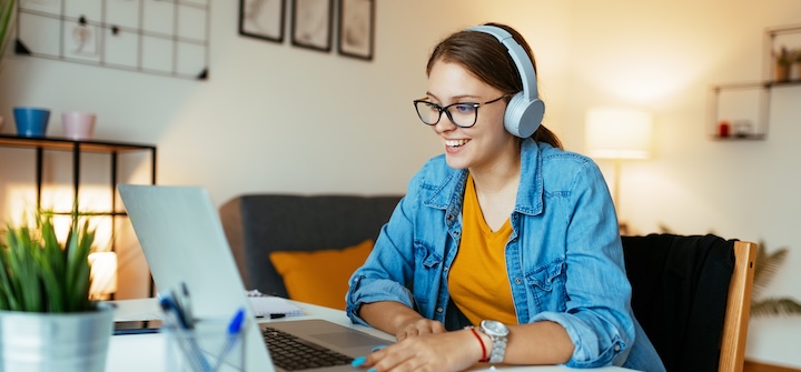 Woman wearing headphones using a laptop in her room