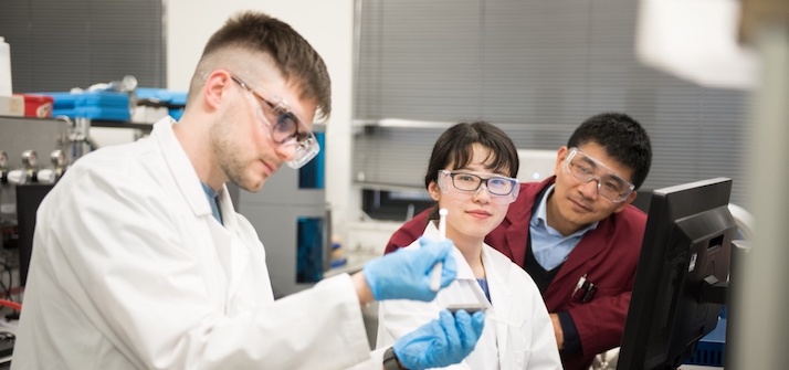 Researcher in a lab carrying out an experiment while another researcher and technician look on