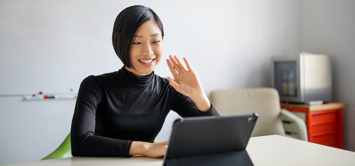Young woman waving while in a virtual meeting on a tablet device