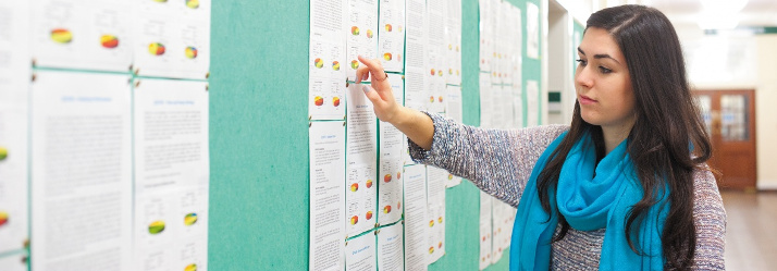 Female undergraduate student looking at a noticeboard, Trent Building 714x249