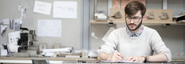 Male undergraduate student working on coursework in The Studio, Architecture and Built Environment Building, University Park 714x249