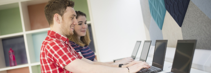 Pair of undergraduate students using laptops in University Park Central Student Service Centre, Cherry Tree Lodge 714x249