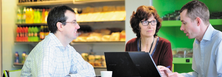 Staff members around a laptop, Medical School cafe 714x249
