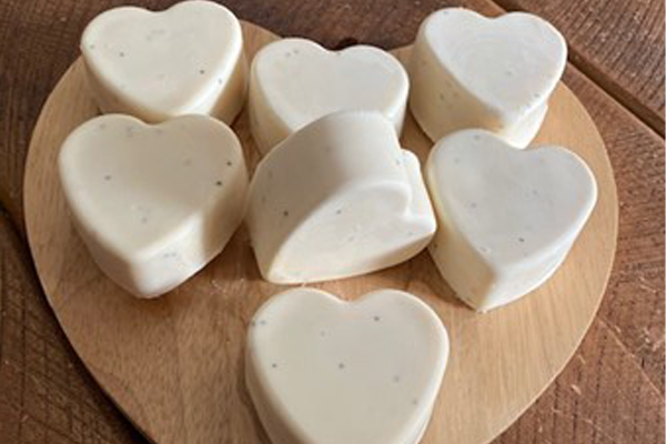 An image of a 7 heart-shaped white bars of hand-made eco-friendly soap on a wooden heart shaped placemat