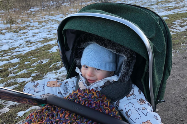 A photo of a smiling young child in a pram, wrapped up in warm clothing, enjoying the view of the sunset and snow on a very cold day