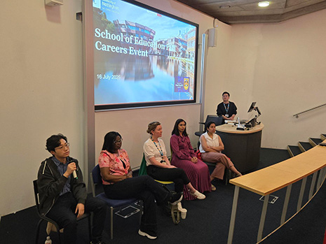 School of Education alumni sitting at front of lecture theatre talking to current MA Students